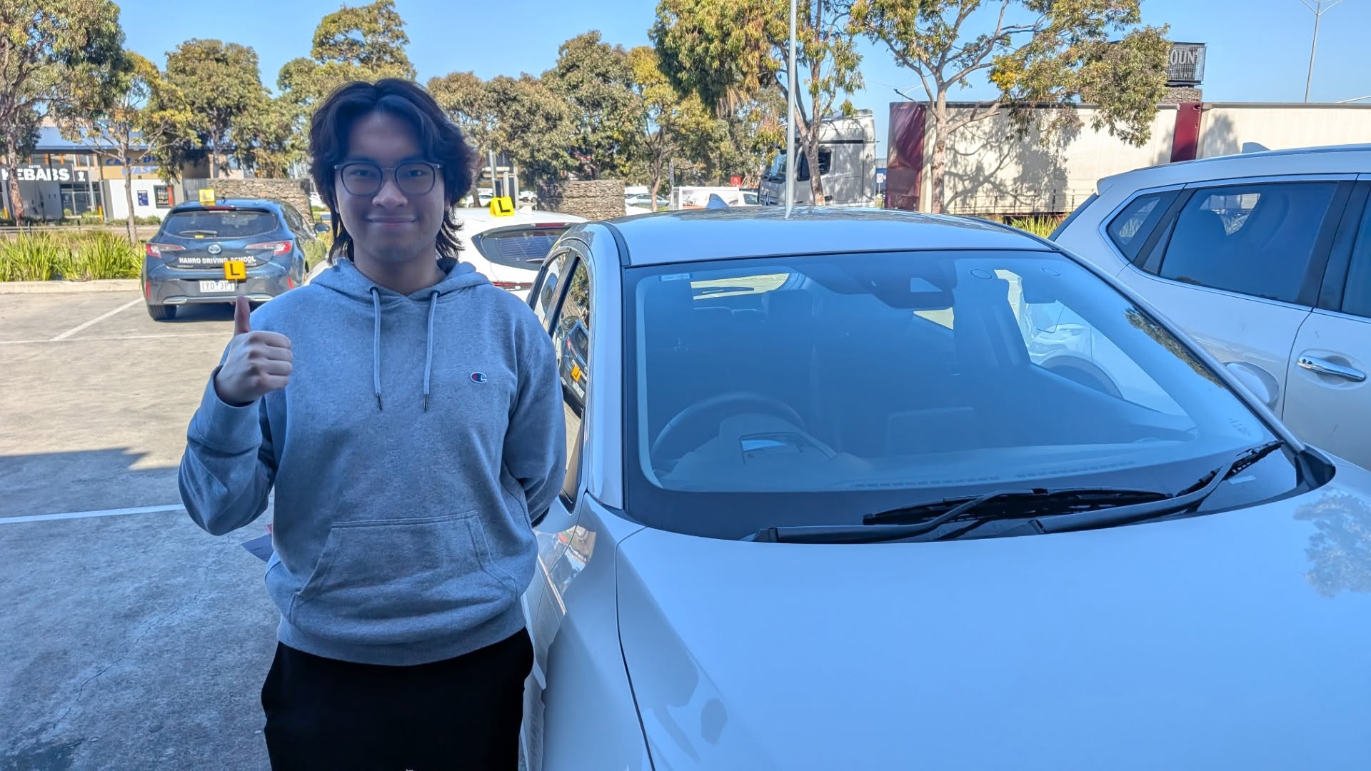 Learner giving a thumbs up beside a white car
