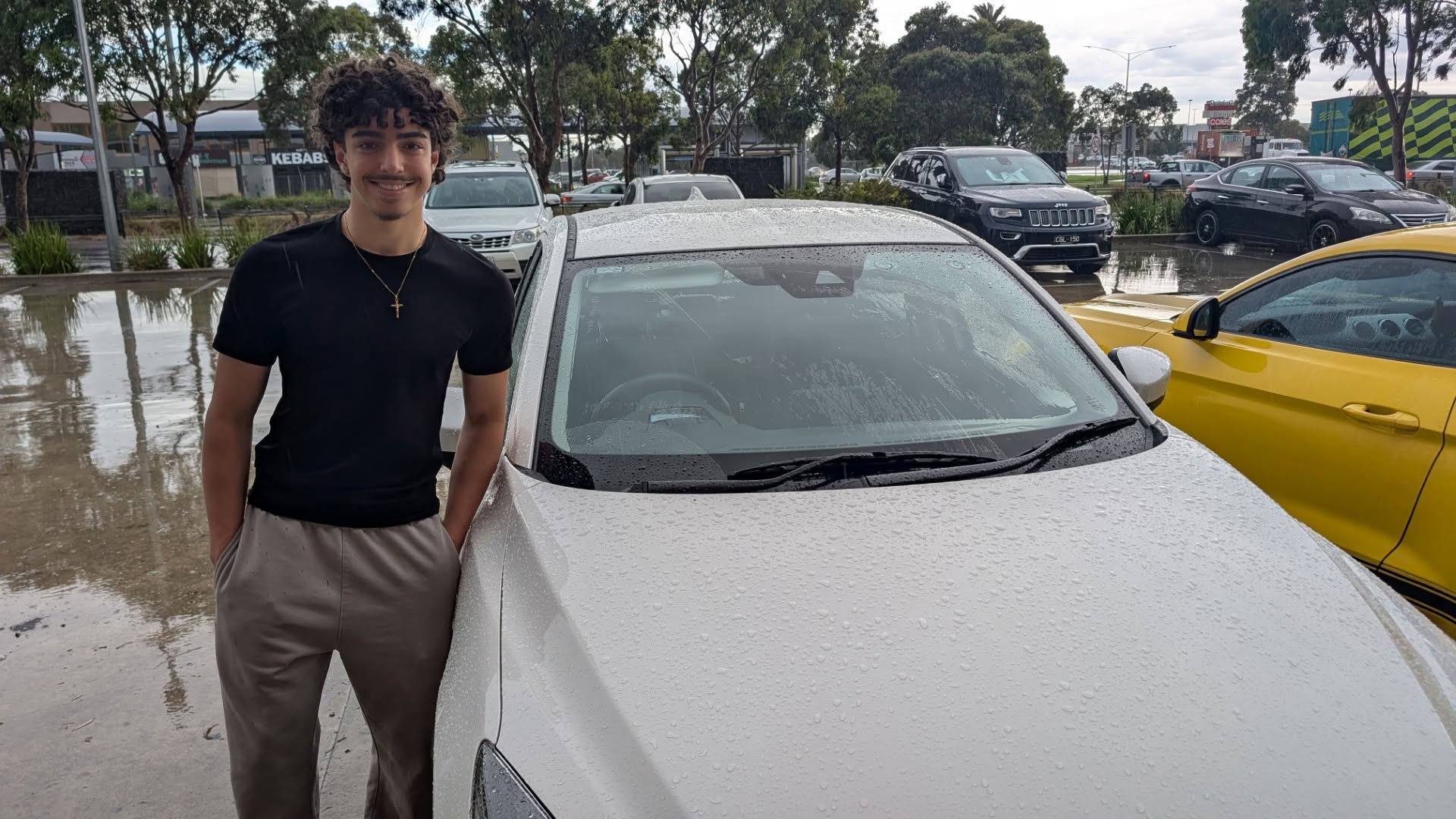 Smiling learner standing beside a white car
