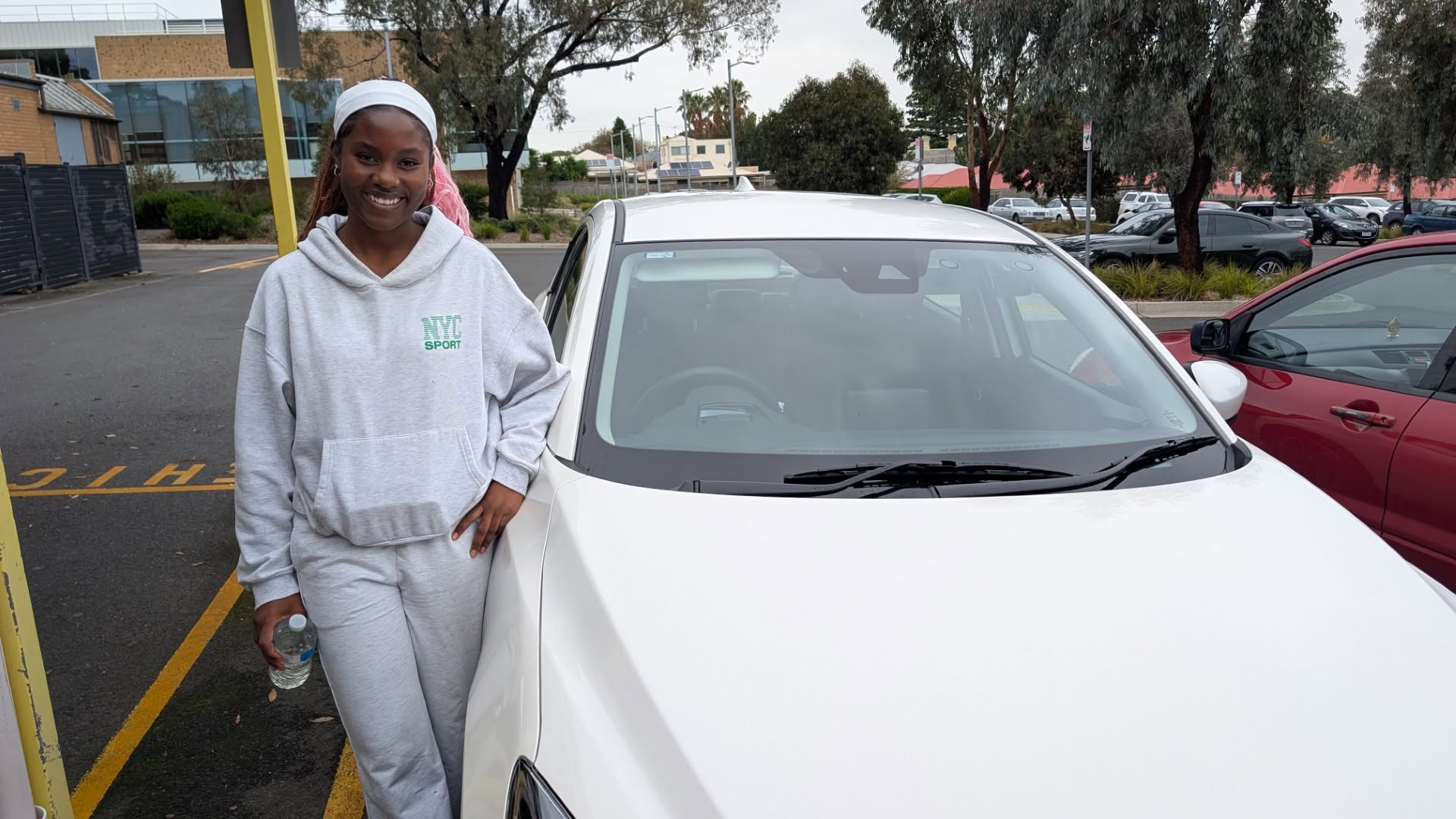 Smiling learner leaning on a white car in a car park